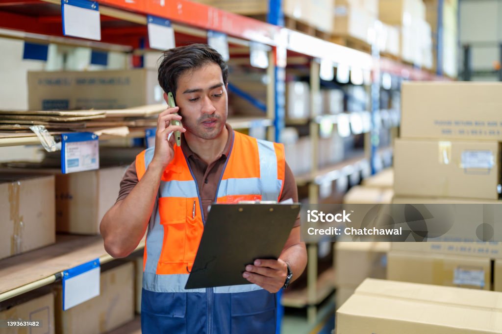 Man warehouse manager using mobile phone talking with customer. Warehouse and Logistic business concept. Man warehouse manager using mobile phone talking with customer. Warehouse and Logistic business concept. Warehouse manager checking the merchandise. Warehouse Stock Photo