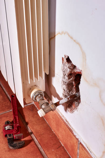 istock Vertical frame. Plumber's faucet in the floor, hole in the wall and heating system leaking water. 1393632950