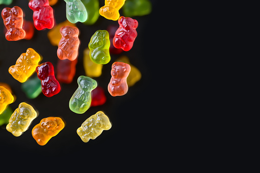 Multicolored flying gummy bears on a black background, flat lay