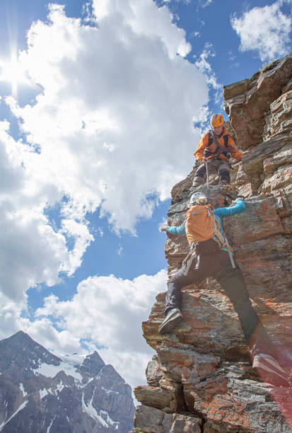 istock Climbing guide assists guest on mountain ridge 1393634847