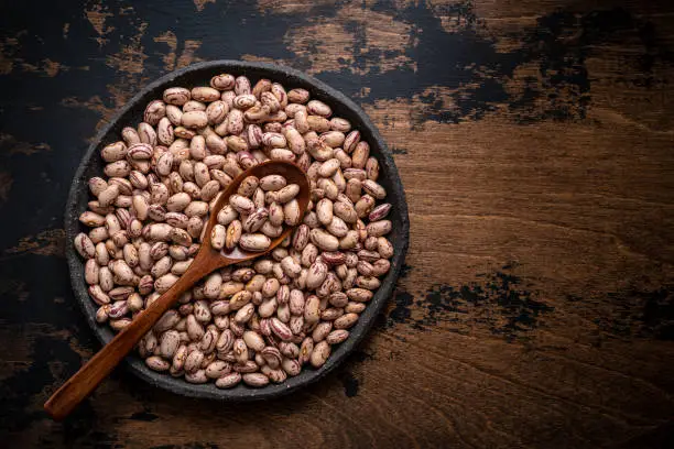 Pinto Beans dried legumes in a plate with spoon on rustic dark wooden background leaving copy space