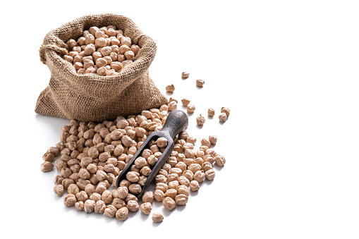 Chickpeas dried legumes in a burlap sack bag and wooden serving scoop isolated on white background leaving copy space