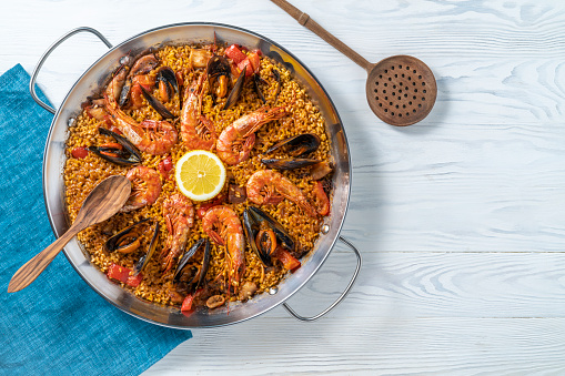 Seafood Paella Mediterranean diet recipe with shrimp, squid and mussels on white wooden background