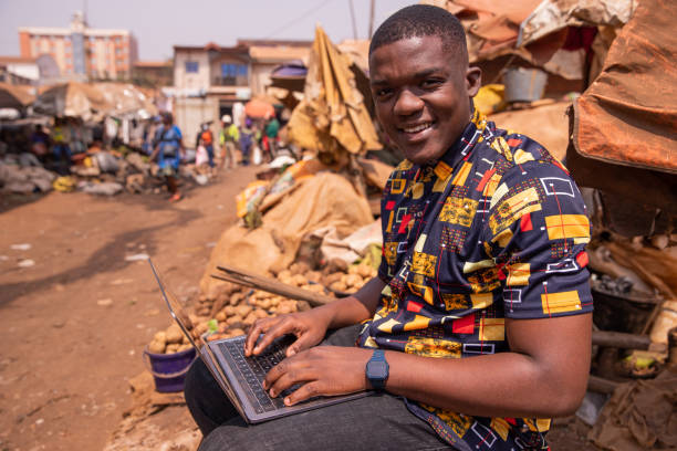 Young african man uses his computer at the market, young people and technology in africa Young african man uses his computer at the market, young people and technology in africa cameroon stock pictures, royalty-free photos & images