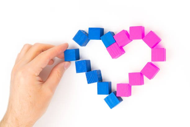 Female hand building a heart shape from pink and blue wooden blocks isolated on white background. Creative charity concept.