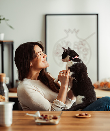 Beautiful smiling woman having breakfast in a dining room. The cat is walking on the table. They are sharing breakfast .