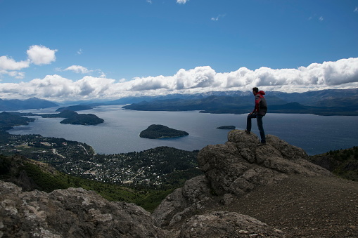 San Carlos de Bariloche is a city in the Argentinian province of Rio Negro. a man on a cliff overlooking the lake and the city of San Carlos de Bariloche. Argentina