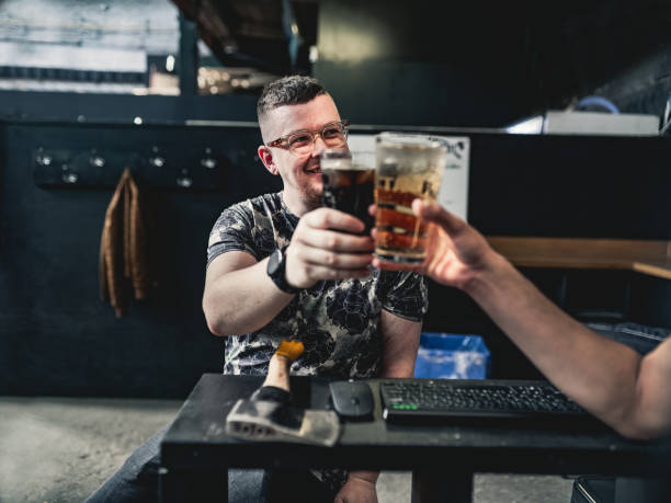 Coupe of young gay man at the axe throwing game room, taking a break from competition. . They are  dressed in casual clothing, wearing eyeglasses. Interior of warehouse like  space during the day.