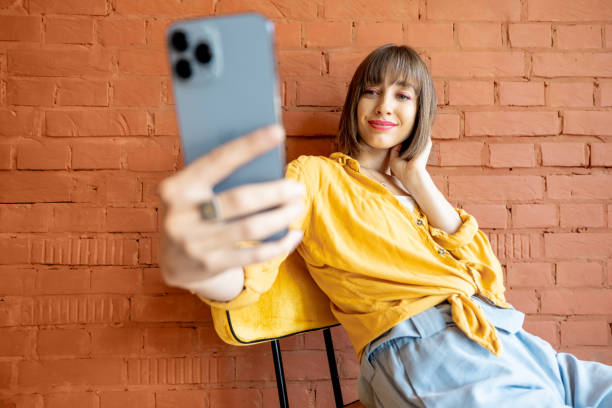 istock Stylish woman with smart phone on brick wall background 1393644891