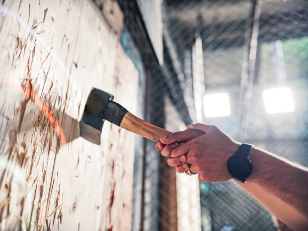 Young gay man throwing axe at the game range Hand of a Young Middle Easter gay man throwing axe at the game range. He is dressed in casual clothing. Interior of warehouse like  space during the day. axe photos stock pictures, royalty-free photos & images