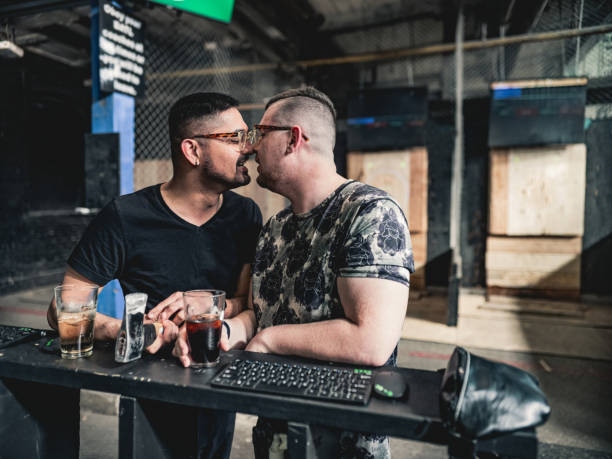 Young gay men at the axe throwing game room Coupe of young gay man at the axe throwing game room, taking a break from competition. . They are  dressed in casual clothing, wearing eyeglasses. Interior of warehouse like  space during the day. axe throwing stock pictures, royalty-free photos & images