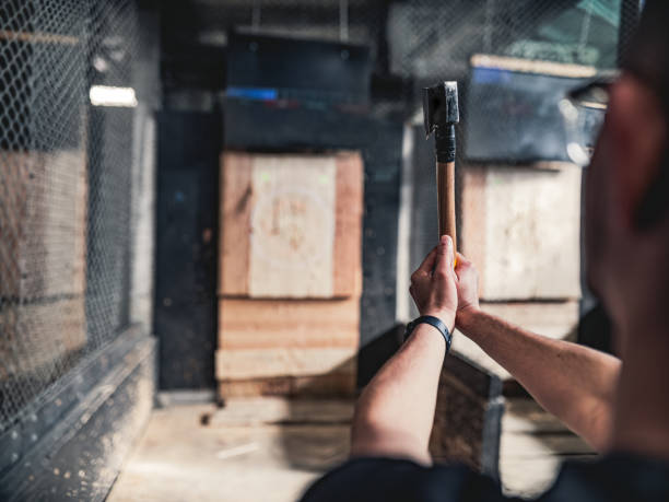 Young gay man throwing axe at the game range Young Middle Easter gay man throwing axe at the game range. He is dressed in casual clothing, wearing eyeglasses. Interior of warehouse like  space during the day. axe throwing stock pictures, royalty-free photos & images