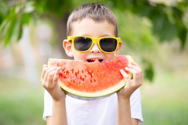 Cute boy in yellow sunglasses eating watermelon outdoors in summer. Healthy eating seasonal berries and fruits Cute boy in yellow sunglasses eating watermelon outdoors in summer. Healthy eating seasonal berries and fruits. yellow melons field stock pictures, royalty-free photos & images