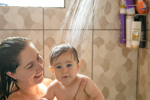 Toddler taking a shower with his mother. Baby boy looking at camera when taking a shower with his young mother.