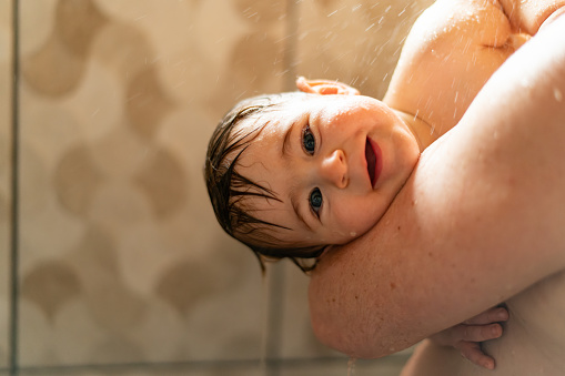 Toddler taking a shower with his father. Baby boy looking at camera when taking a shower with his father.