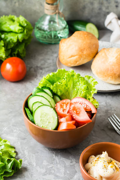 Fresh vegetable bowl with cucumber, tomato and lettuce on the table at home. Vegetarian healthy food. Vertical view. Close-up