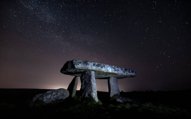 Lanyon Quoit, Cornwall, UK Situated in largely unpopulated and treeless Cornish landscape between Madron and Morvah, Lanyon Quoit, along with other Cornish dolmens, dates back to the Neolithic period (3500-2500BC), predating both the pyramids in Egypt and metal tools.

The original use is somewhat disputed; some believing that it was the burial chamber of a large mound and others contesting that it was never completely covered, but rather used as a mausoleum and the imposing backdrop to ritual ceremonies, especially since it is believed that in its original form the quoit was aligned with cardinal points. Another theory is that bodies were placed on the capstone to be eaten by carrion birds. Nearby lie a number of small stone burial chambers, knows as cists, with a longstone about 100 yards north-west of the quoit and evidence that there were once a number of neighbouring barrows.

Once tall enough to allow a horse and rider to pass underneath, Lanyon Quoit is certainly one of Cornwall’s most recognisable and important megalithic sites. The mammoth capstone, weighing over 13 tonnes and measuring 9 feet by 17 feet, originally sat atop four upright stones until a thunderstorm in 1815 dislodged it. Attributed in part to soil removal from numerous treasure hunting explorations, the fall broke one of the supporting stones, hence the diminished stature achieved when re-erected by local public subscription (incidentally, the equipment used to replace the capstone was that previously used to replace the Logan Rock). igneous rock stock pictures, royalty-free photos & images