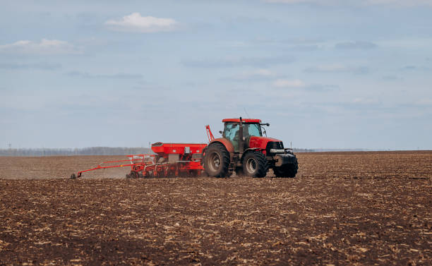 istock Spring sowing season. Farmer with a tractor sows corn seeds on his field. Planting corn with trailed planter 1393673556