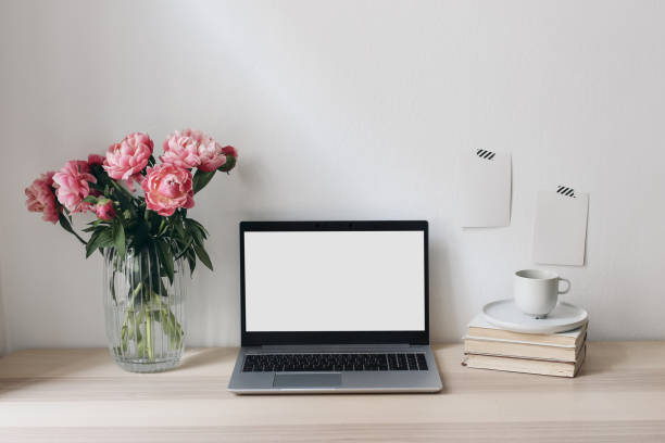 istock Home office still life scene. Notebook, computer and memo cards mock-ups. Vase with pink peonies flowers, books and cup of coffee. Wooden table. Elegant feminine working space. Living room interior. 1393673671