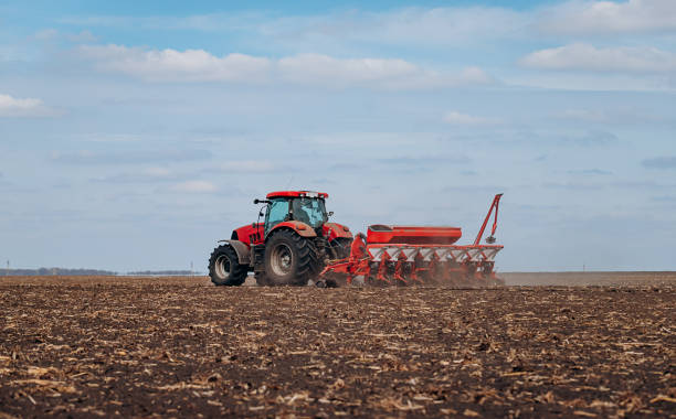 istock Spring sowing season. Farmer with a tractor sows corn seeds on his field. Planting corn with trailed planter 1393673760