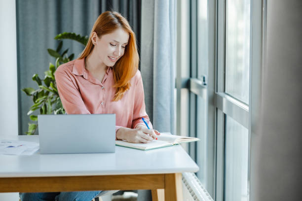 istock Young redhead woman using laptop and writing notes 1393677946