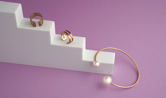Gold with pearls bracelet and rings on white podium on violet color background with copy space