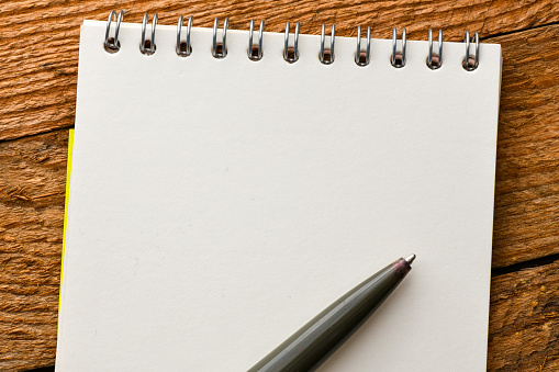 Horizontal picture of a white page of a single lined spiral bound notepad. The punch holes of the note pad are round and the spiral wire is black in colour. There is a blank plain paper sheet below by the notepad. There is no text, no people and ample copy space.