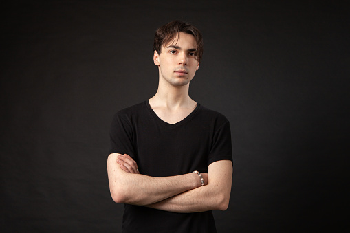 Studio portrait of a 20 year old man with brown hair in a black t-shirt on a black background