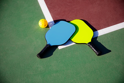 This is a photograph taken outdoors on location of two pickleball paddles and balls at the corner edge of the court