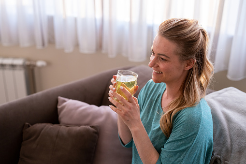 Happy woman sitting on sofa at home and holding juice