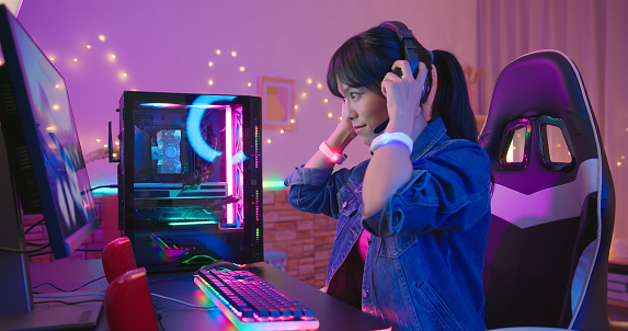 side view of young asian pretty pro gamer wearing on headset and ready to play in online video game at home