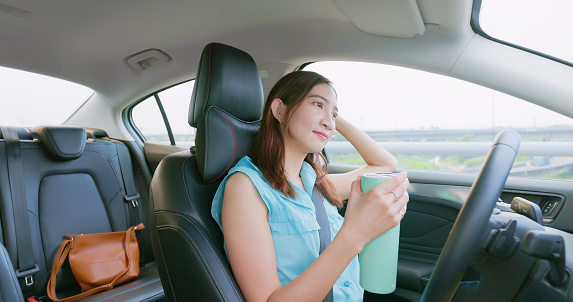 relaxed asian woman experiences riding autonomous self driving car and drinking on highway