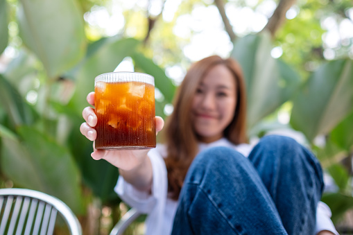 Blurred image of a young asian woman holding and showing a glass of iced coffee