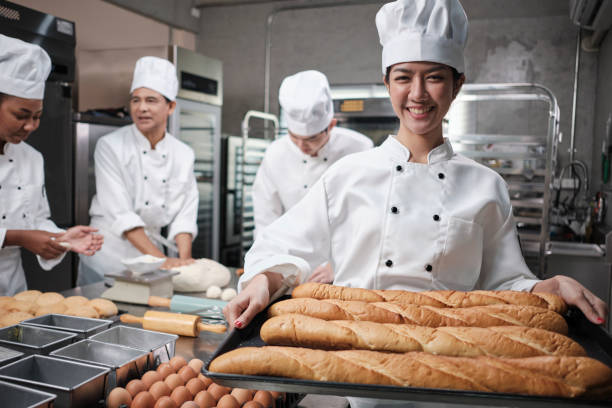 istock Professional Asian female chef with baking baguette, cheerful smile in kitchen. 1393727384
