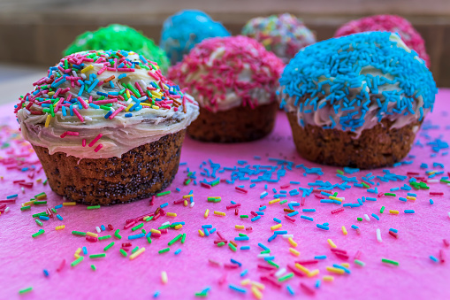 Close-up of homemade cupcakes decorated with white frosting and multi colored sugar sprinkles on pink table