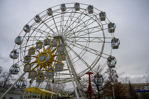 A large Ferris wheel with closed cabins for resting people and a musical clock in the middle in the Tyumen Culture Park (Siberia, Russia). close-up. Summer cloudy day