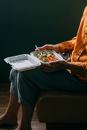 An anonymous Caucasian woman eating some salad she has ordered from her favourite restaurant.