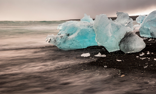amazing blue colored icebergs washed ashore the black sand beach commonly named Diamond Beach in Iceland.