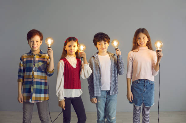 istock Group of happy creative children standing in studio and holding shining light bulbs 1393751290