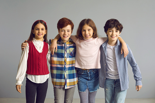 Little boys and girls making friends and having fun together. Happy kids huddling and smiling at camera. Studio group portrait of school children standing in row with arms on each other's shoulders