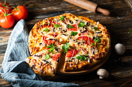 Close-up on baked pizza dough with fresh mortadella slices, mozzarella and pesto sauce condiment on top