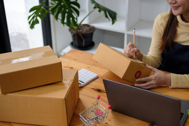 Starting small businesses SME owners female entrepreneurs writing address on receipt box and check online orders to prepare to pack the boxes, sell to customers, sme business ideas online. inicio de pequeñas empresas propietarios de pymes mujeres empresarias escribiendo la dirección en la caja de recibo y verificando los pedidos en línea para prepararse para empacar las cajas, vender a los clientes, ideas de negocios de pymes en línea