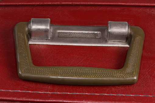 Handle made with plastic and metal of the old red leather substitute hard-shell suitcase, top view close-up