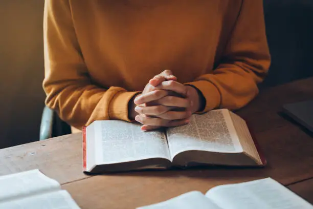 Photo of Women's hands clasped together on her Bible praying to god. believe in goodness. Holding hands in prayer on a wooden table. Christian life crisis prayer to god.