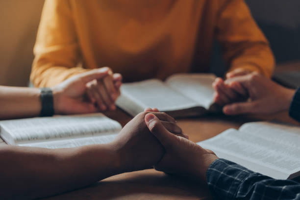 Christian family holding hands praying worship believe and seeking the blessings of God, fellowship, or bible study concept. They were reading the Bible and sharing the gospel. stock photo