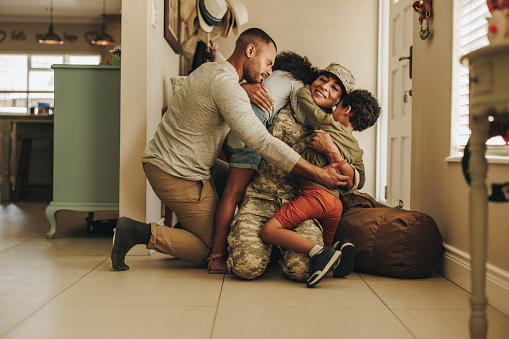 Cheerful military homecoming. Female soldier reuniting with her husband and children after serving in the army. Servicewoman embracing her family after returning home from deployment.