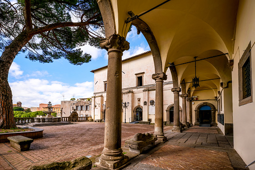 A suggestive view of the courtyard and the porch of the Palazzo dei Priori, in the medieval heart of Viterbo, in central Italy. Built in 1264 as the seat of the civic government, the Palazzo de Priori was also used over the centuries as the seat of the Papal government. The current Renaissance-style structure was built in 1460 while the portico was built in 1541. Currently the Palazzo dei Priori is the seat of the Municipality of Viterbo (Town Hall). The medieval center of Viterbo, the largest in Europe with countless historic buildings, churches and villages, stands on the route of the ancient Via Francigena (French Route) which in medieval times connected the regions of France to Rome, up to the commercial ports of Puglia, in southern Italy, to reach the Holy Land through the Mediterranean. Located about 100 kilometers north of Rome, in the Lazio region, Viterbo is also known as the City of Popes because in the 13th century it was the seat of papal power for 24 years. Founded by the Etruscan civilization and recognized as a city in the year 852, Viterbo is characterized by its peperino stone and tuff constructions, materials abundantly present in this region of central Italy. Super wide angle image in high definition format.