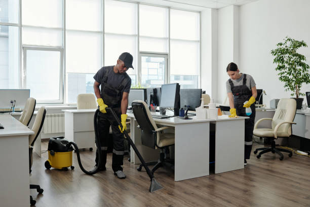istock Young black man in workwear cleaning floor while girl wiping desks with computers 1393767076