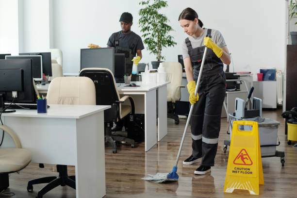 giovane uomo di colore che pulisce i monitor del computer mentre la donna con la scopa pulisce il pavimento - floor wet slippery danger foto e immagini stock