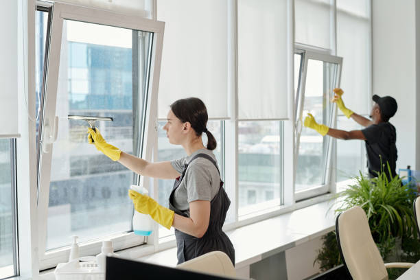 istock Young female cleaner in workwear washing large windows of openspace office 1393767113